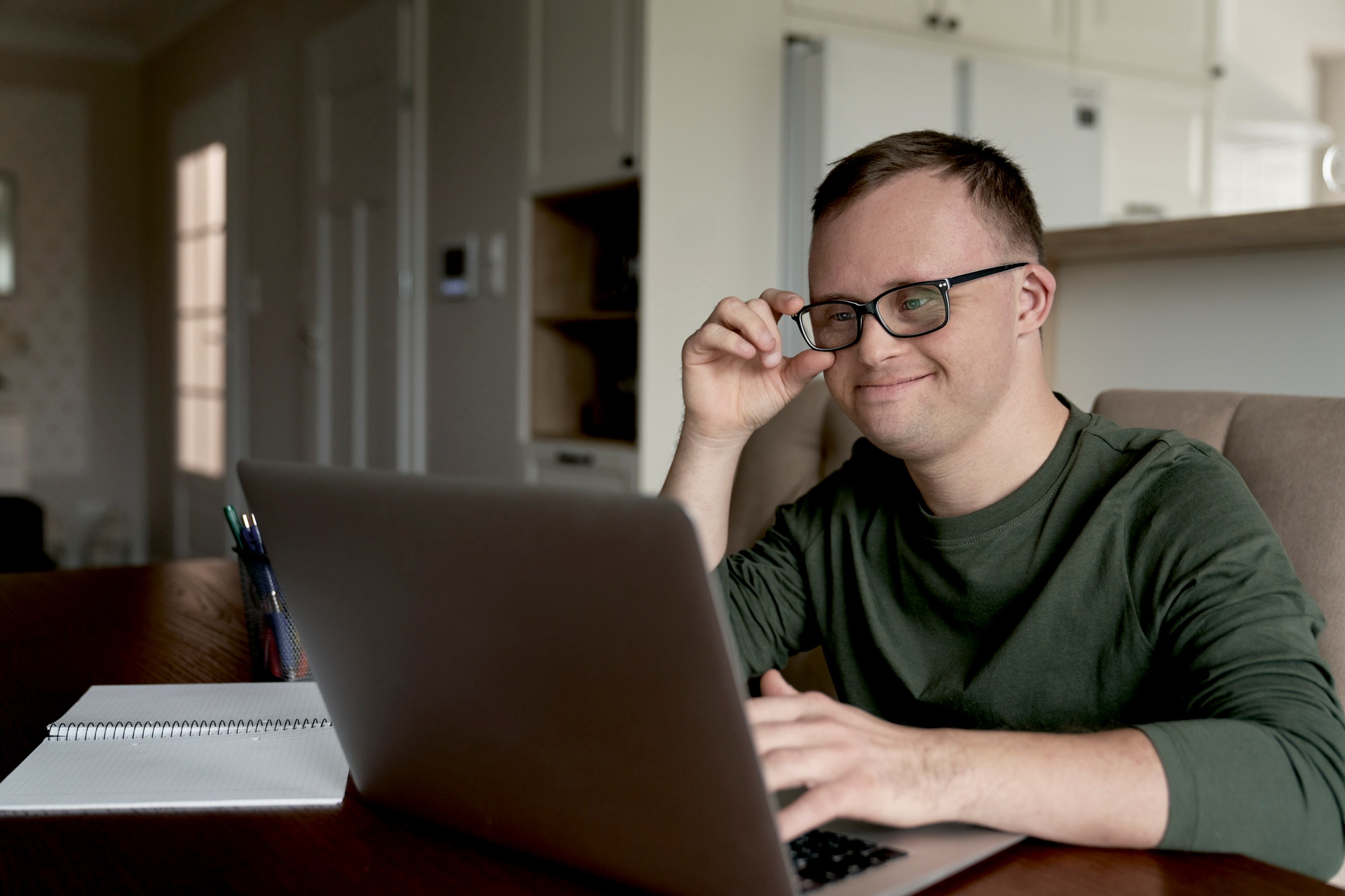 Cheerful adult man with down syndrome using laptop at home