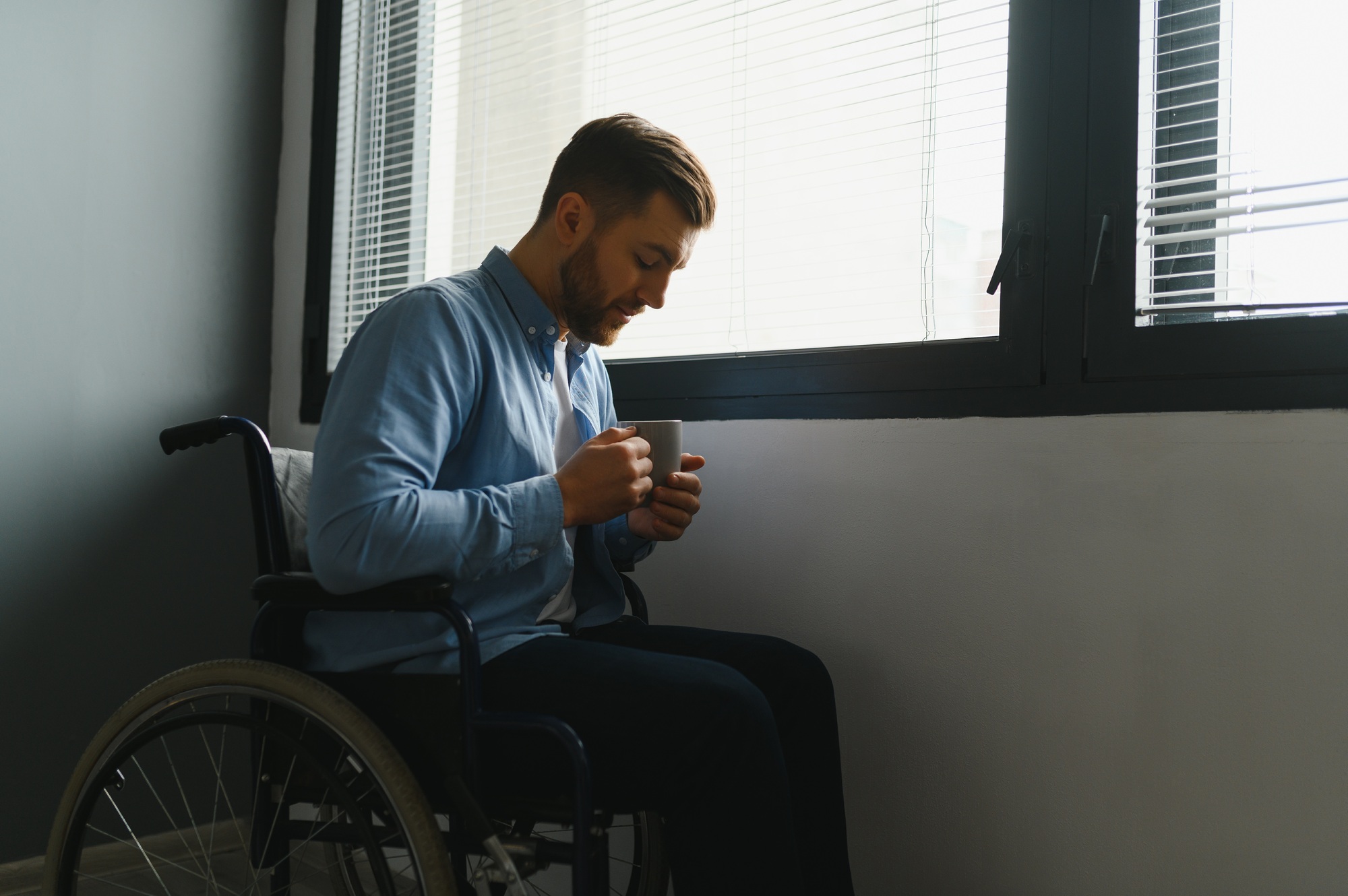 Disabled Person Sits in Wheelchair Against Window.