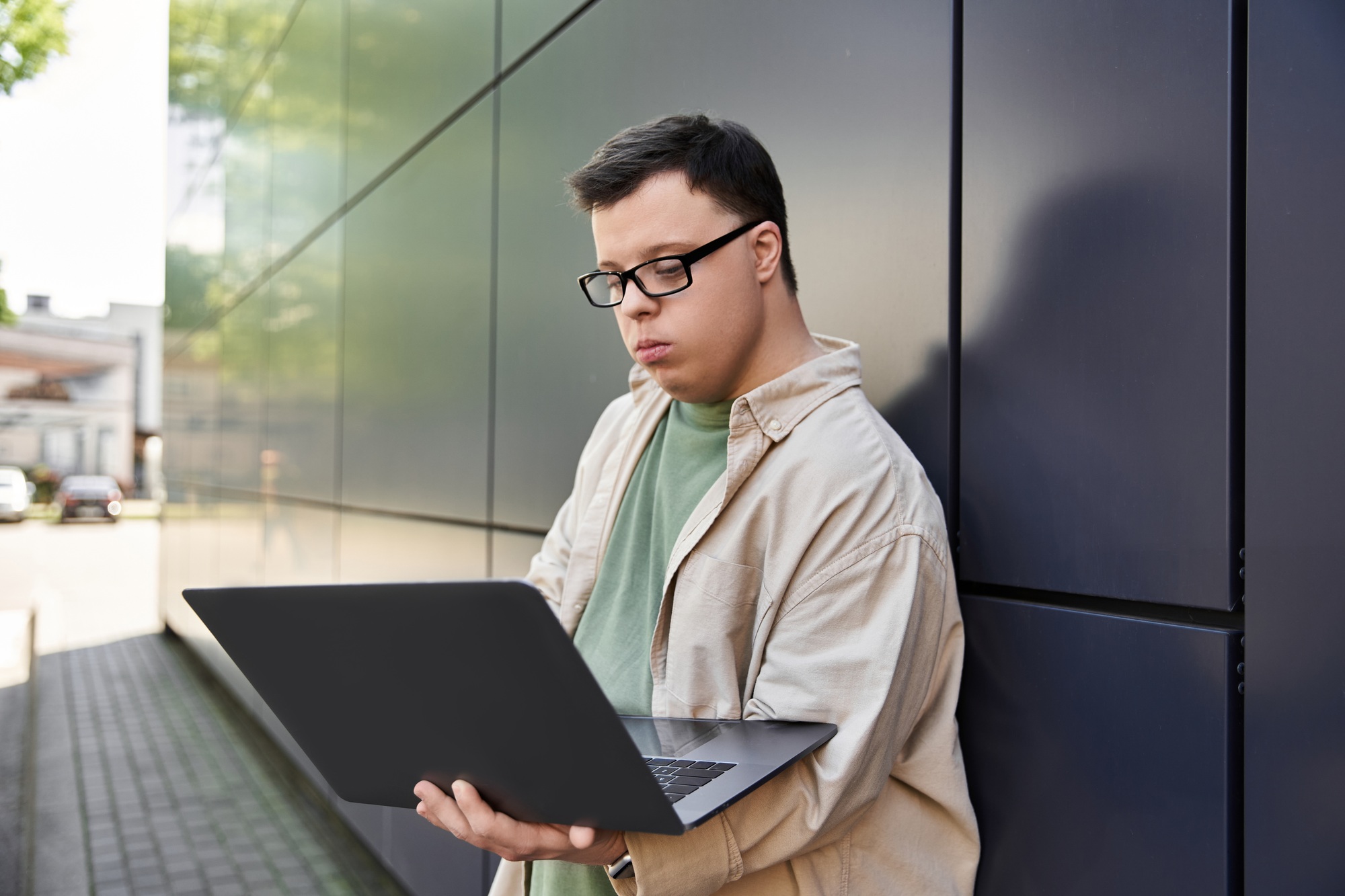 Young Man With Down Syndrome Uses Laptop in Urban Setting
