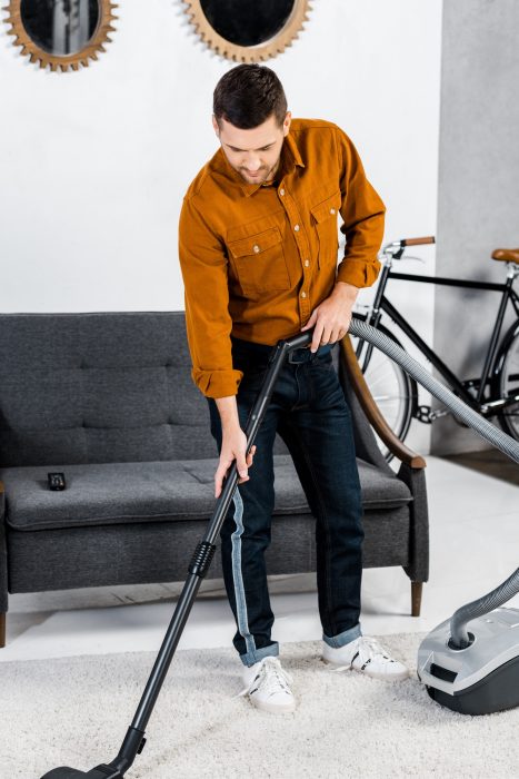 handsome man in modern living room cleaning house with hoover